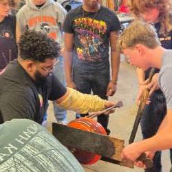 An artist works on a piece of glass art with several students